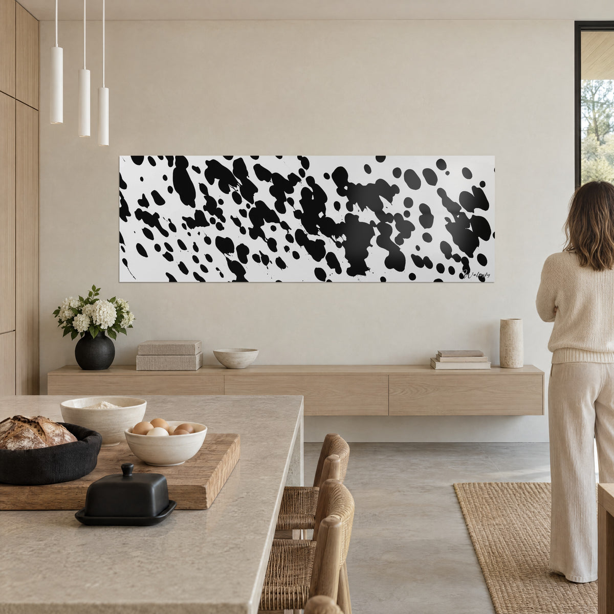 Cuadro con chorros de tinta negra y blanco lechoso, gran formato alargado, pared beige, cocina abierta de madera rubia y encimera