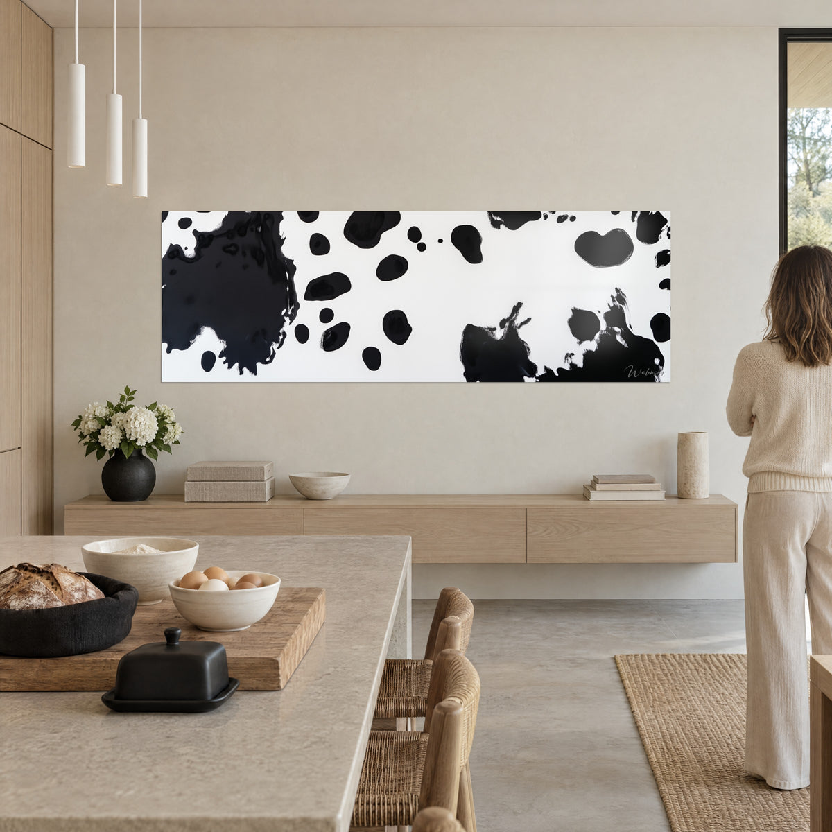 Schilderij met zwarte inktuitbarstingen op wit canvas, grafische en contrasterende vacht, als achtergrond van een open keuken, vrouw van achteren