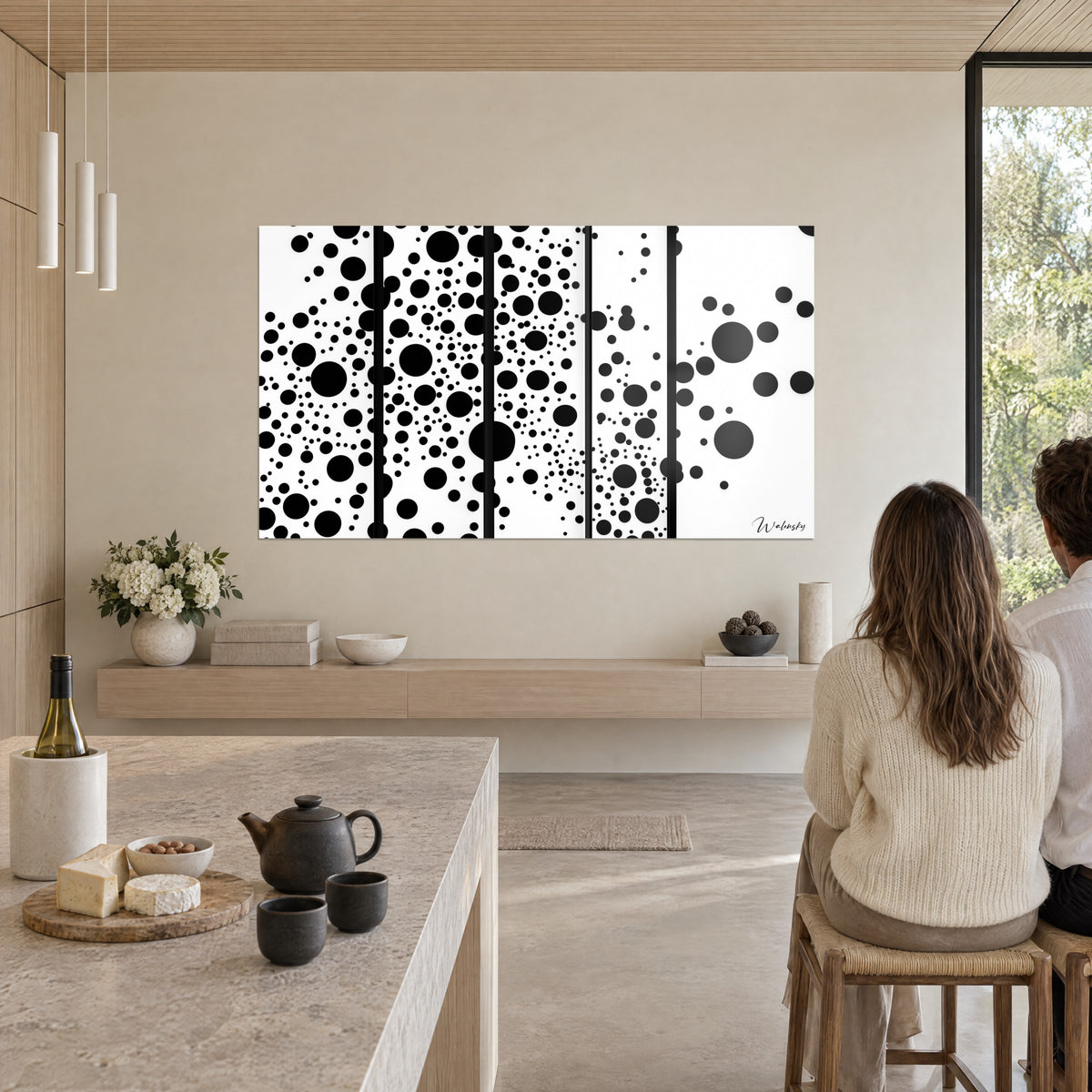 Tableau nuée de disques noirs sur blanc, cinq panneaux, deux personnes de dos attablées près d'un îlot de cuisine en pierre claire