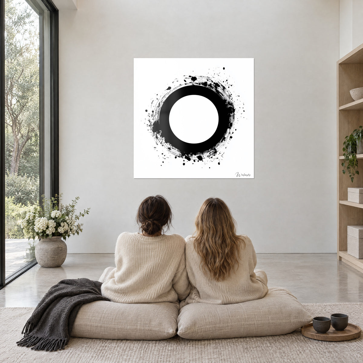 Cuadro ensō minimalista negro sobre blanco, salpicaduras finas, dos mujeres de espaldas sobre cojines beige frente a un ventanal