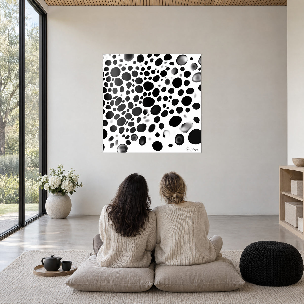 Wall art with rain of black and grey spots on pure white background, two women seen from behind seated on cushions, bright cream wall