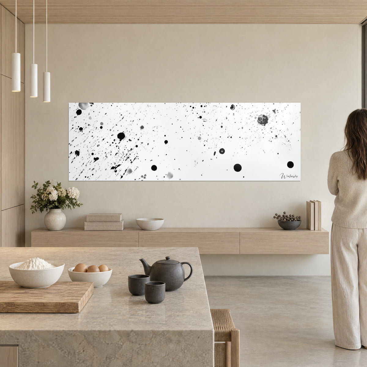 Gemälde mit einem Nebel aus schwarzen Punkten und grauen Lichthöfen auf Weiß, beige Wand, stehende Frau in Elfenbein, Insel aus hellem Stein, offene Küche