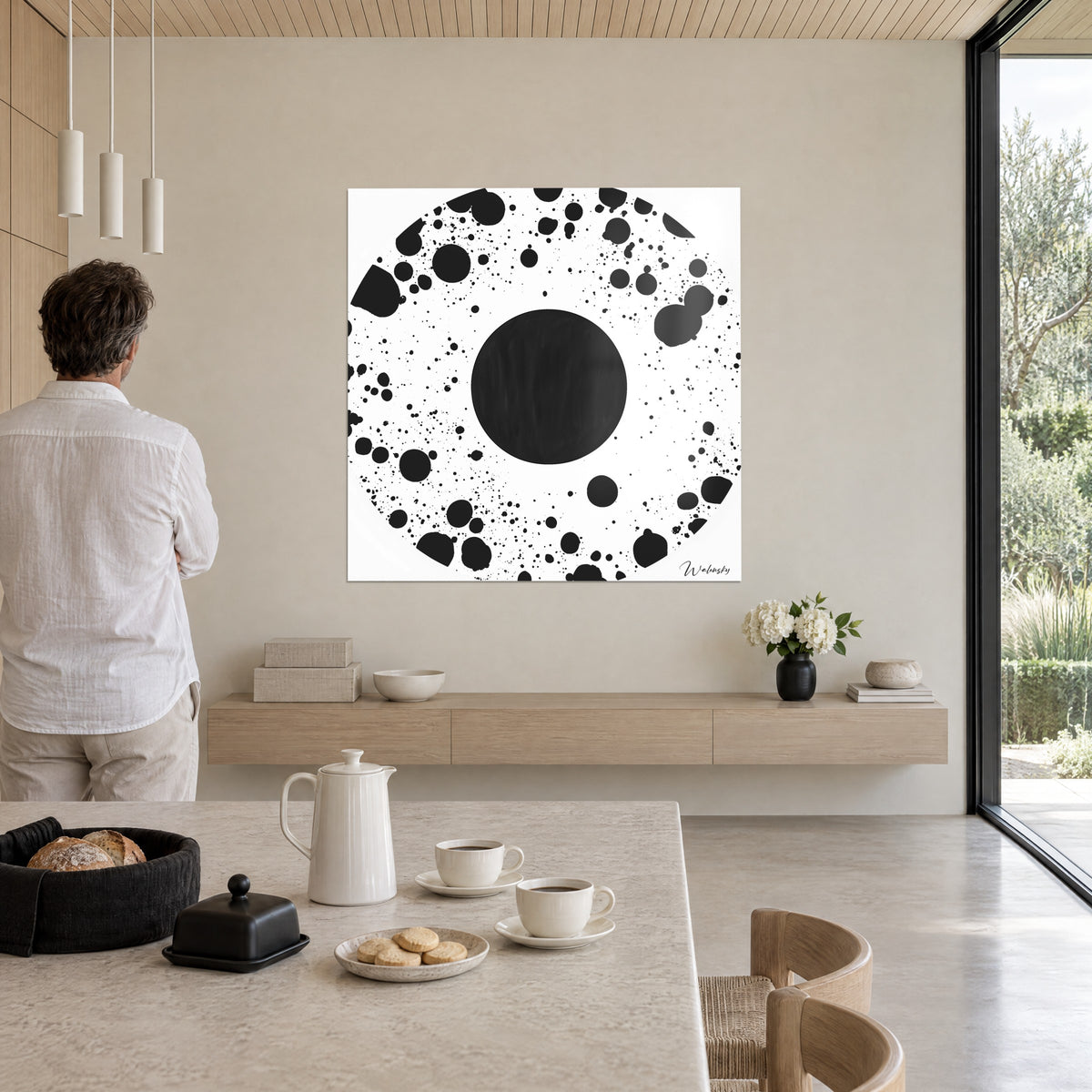 Tableau explosion d'encre noire autour d'un grand rond sombre sur blanc, un homme en chemise claire de dos, dans une pièce de vie ouverte sur le jardin