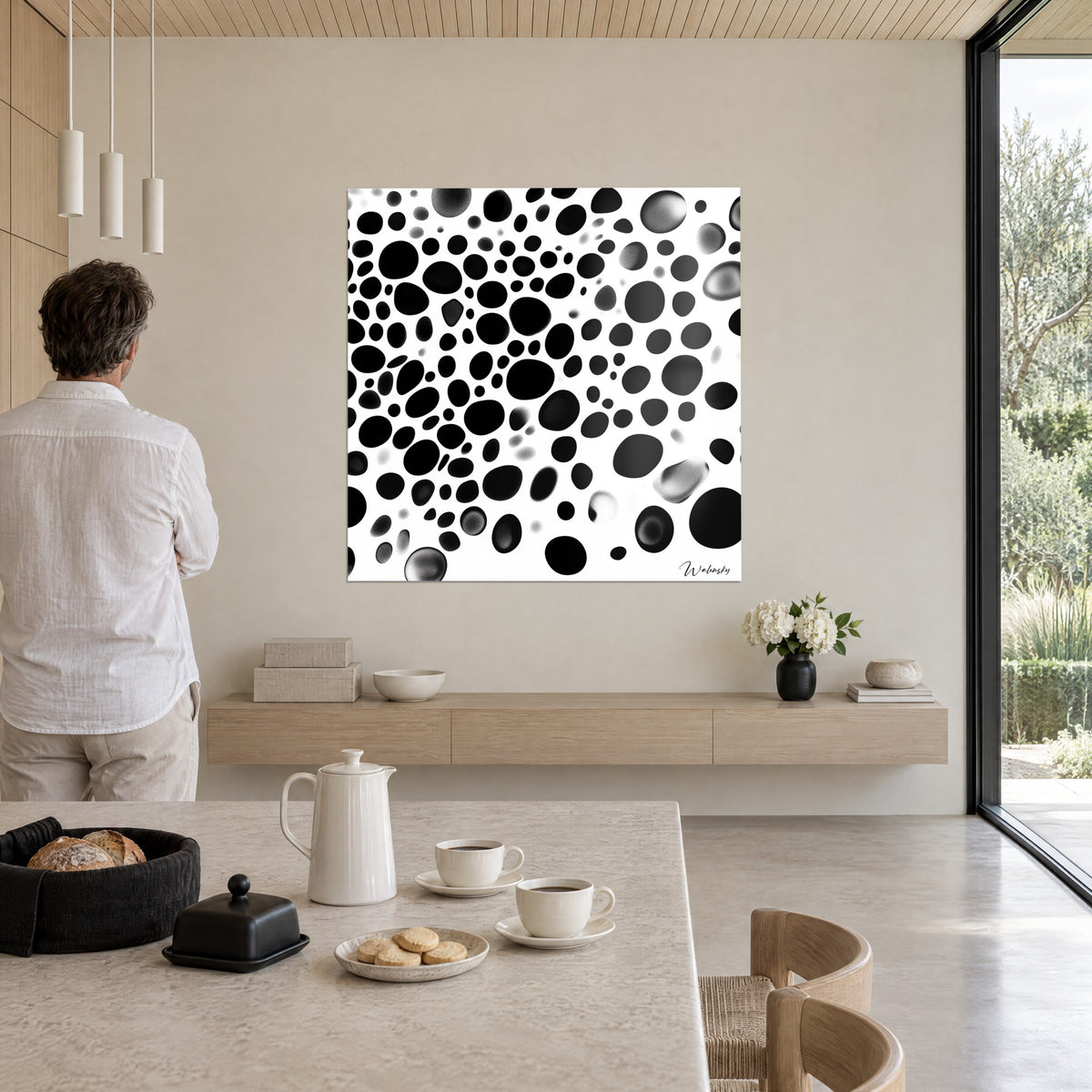 Wall art with organic drop pattern in deep black and ash grey on white, a man in a light shirt seen from behind, living room opening onto the garden