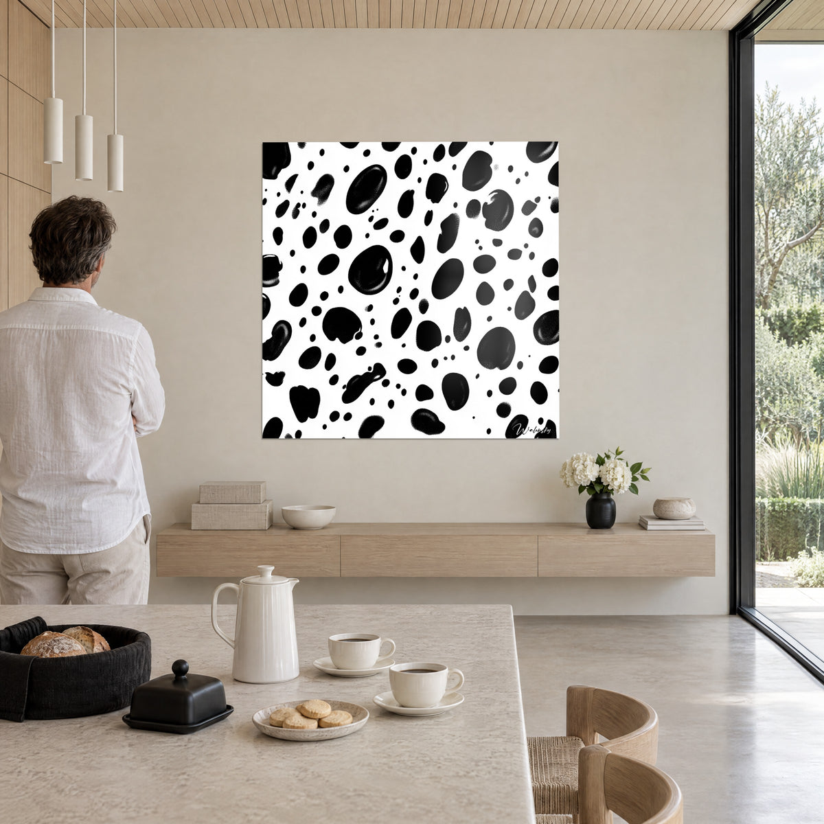 Cuadro con guijarros negros esparcidos sobre blanco radiante, manchas ovaladas irregulares, en la pared beige de un salón abierto a la naturaleza