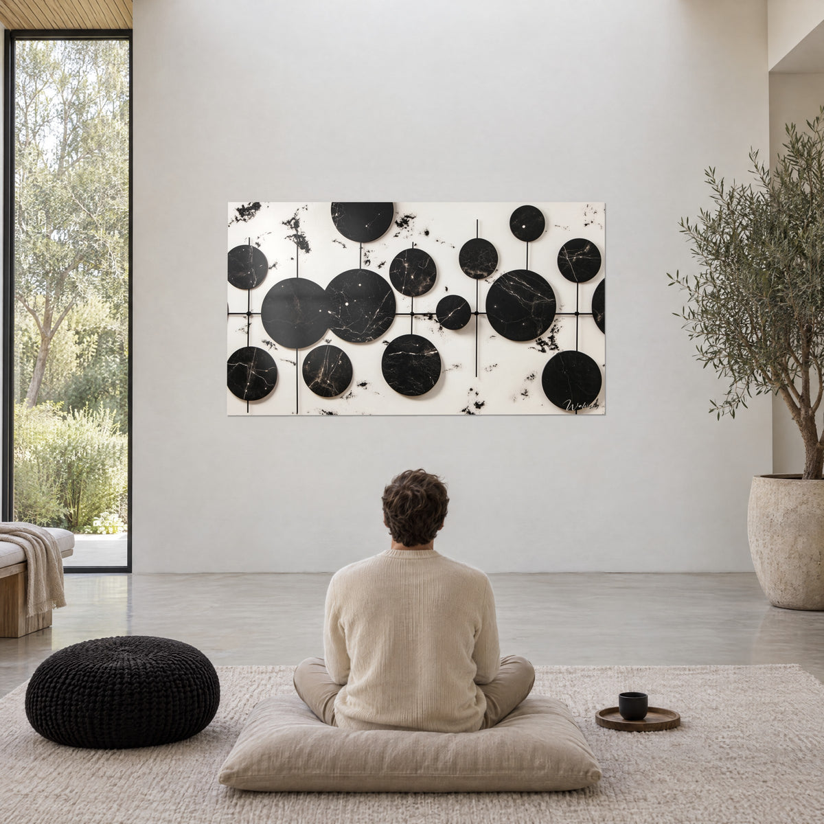 Cuadro de galaxia de medallones negros veteados de blanco, salpicaduras de tinta sobre fondo crema, un hombre de espaldas sentado en meditación sobre un cojín beige