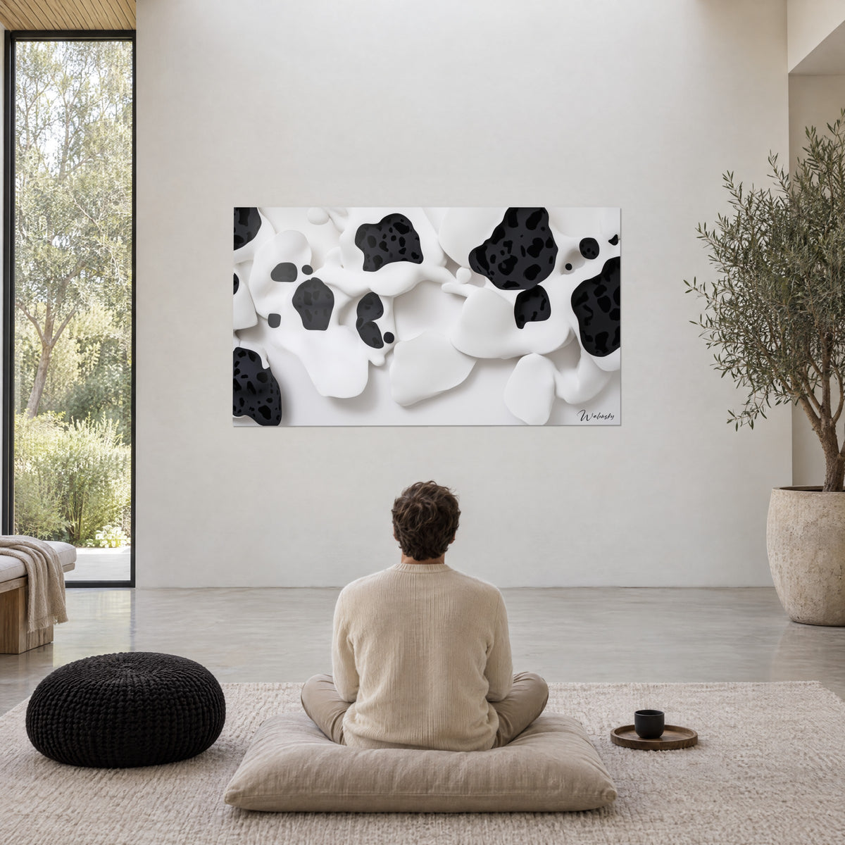 Quadro con rilievi lattiginosi maculati di inchiostro nero, un uomo seduto a gambe incrociate su un cuscino beige, di spalle, in un soggiorno luminoso