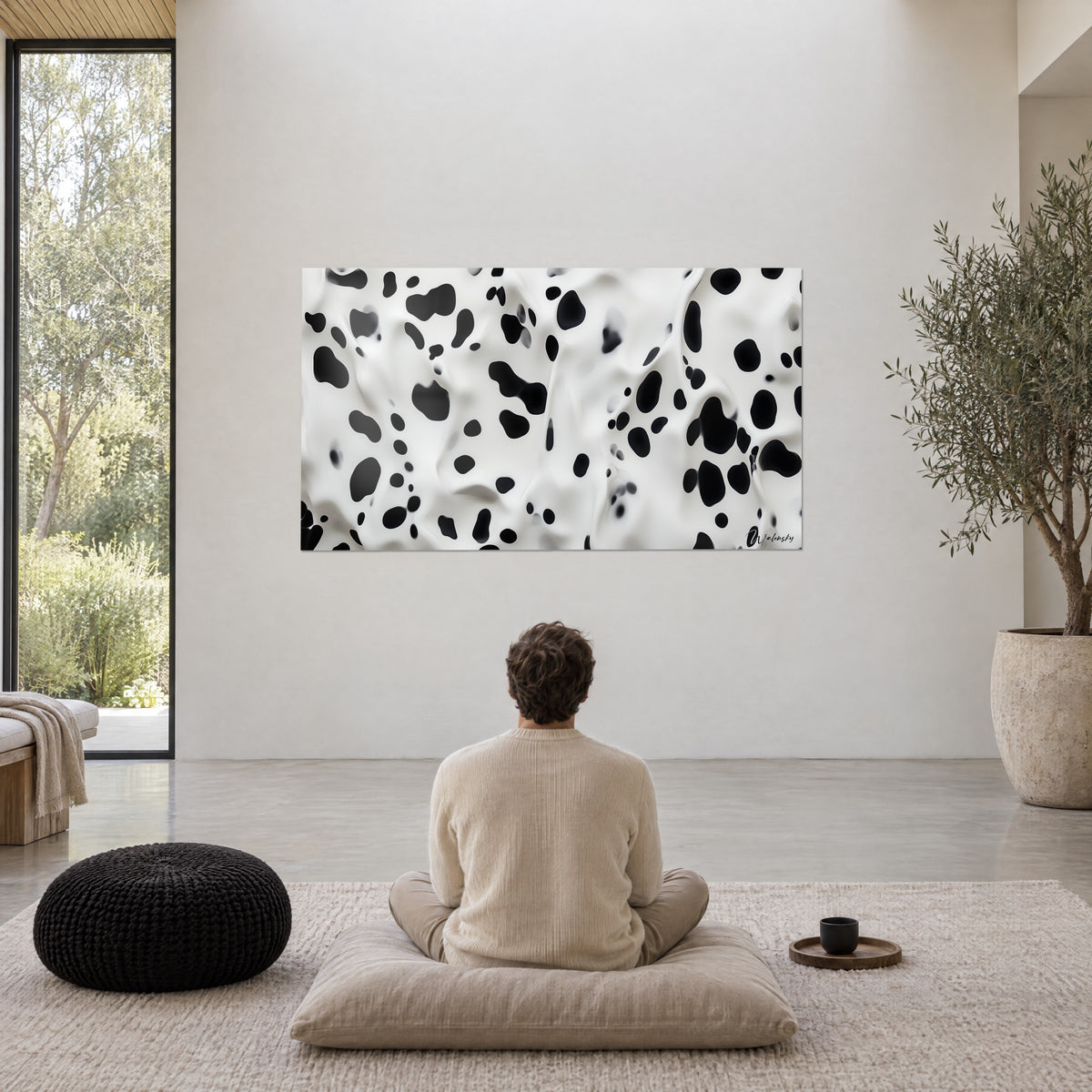 Tableau textile moucheté noir et blanc aux plis souples, homme de dos assis en méditation sur un coussin dans un séjour clair aux murs beiges