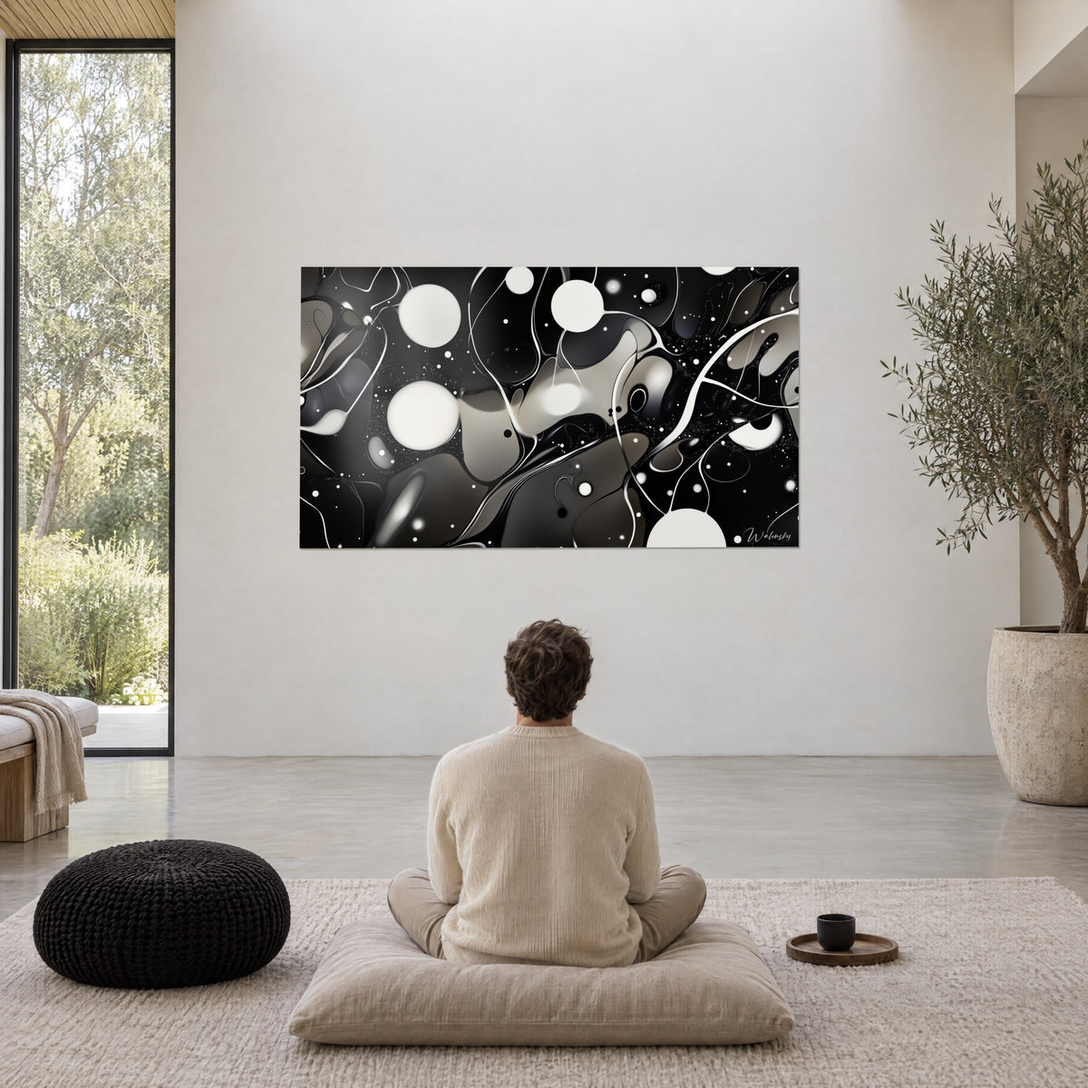 Wall art white orbs floating over black and grey stains, white wall, potted olive tree, man seated in meditation