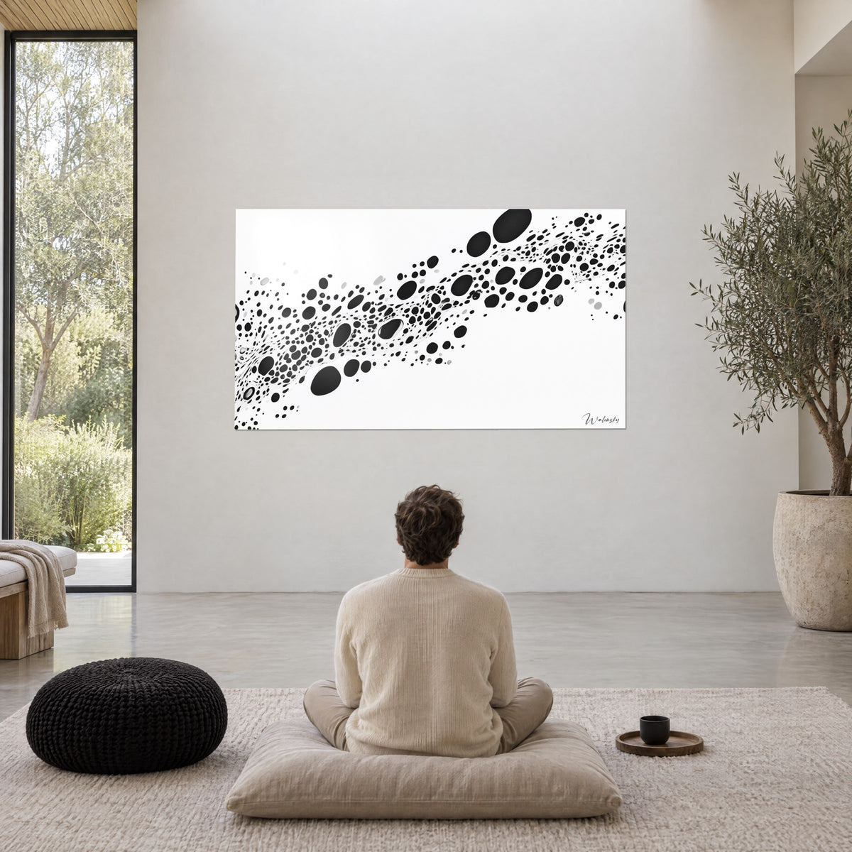 Tableau flot de cellules noires sur fond blanc lumineux, homme de dos en pull crème assis sur un coussin gris, olivier dans un grand pot