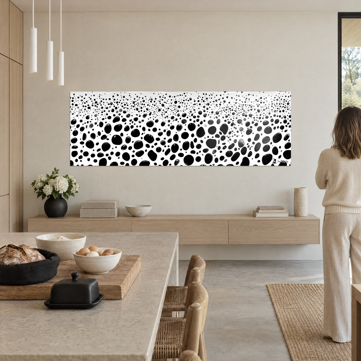 Cuadro con motivo moteado en blanco y negro, burbujas ovaladas y lisas, una mujer de espaldas mira la tela junto a una isla de cocina de madera