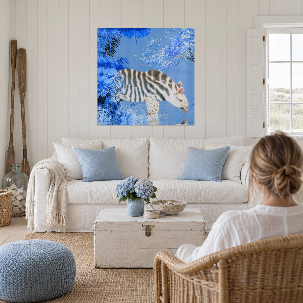 Gemälde Tapir in Weiß mit graubraunen Streifen, trinkend in blauem Wasser unter gefrorenen Blüten, über einem Sofa in einem hellen Wohnzimmer