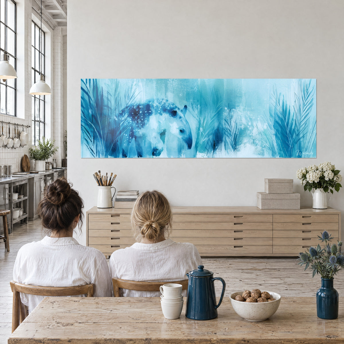 Tableau tapir bleu glacier et palmes cyan, deux femmes de dos attablées face au mur du loft d'artiste, buffet clair