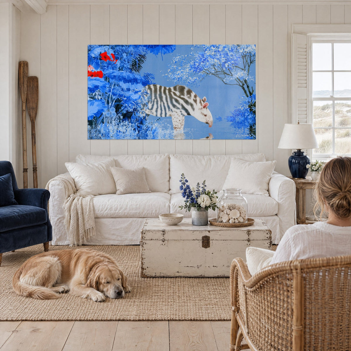 Wall art of a young striped tapir drinking from blue water, red flowers, resting retriever, above a sofa in a bright living room