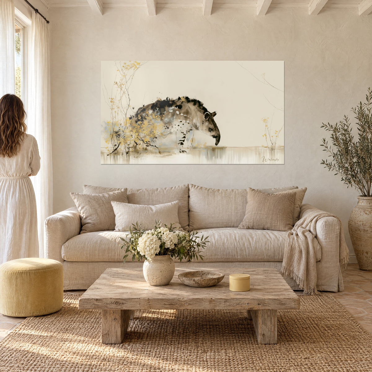 Wall art tapir in brown and ochre ink, muzzle lowered toward the water, golden branches, above a sofa in a bright living room