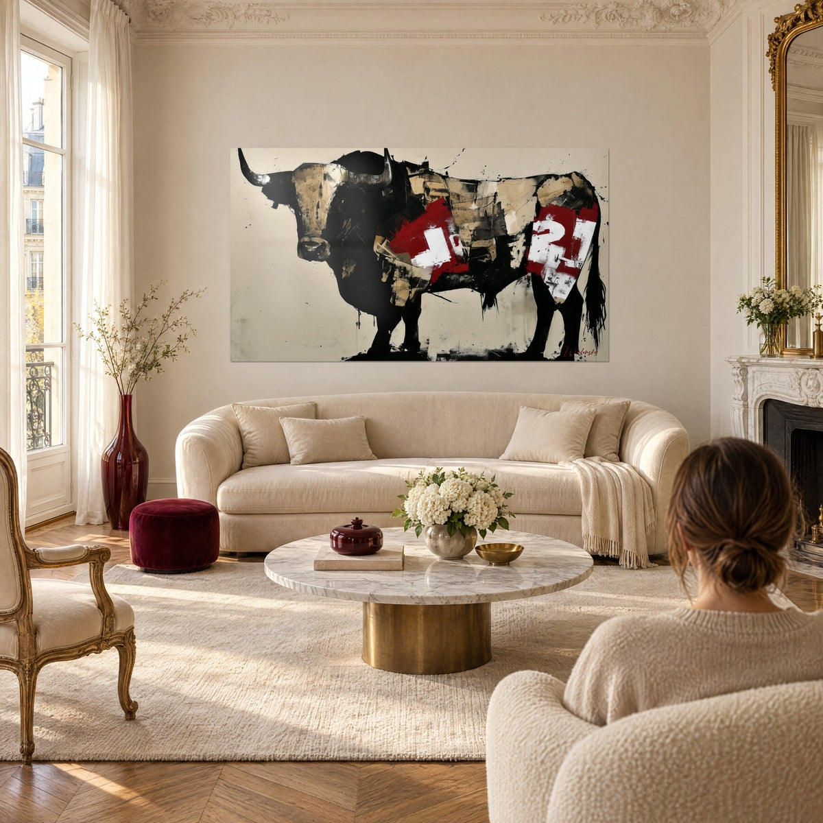 Wall art black Longhorn with curved horns, red and beige collage on the flank, woman seen from behind, above a sofa in a bright living room