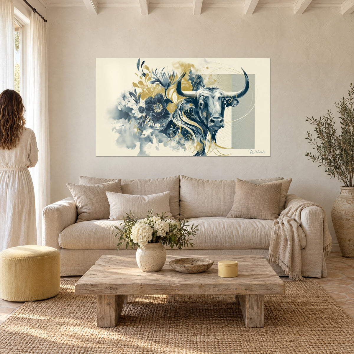 Wall art of a bull with long black horns, navy blue flowers and gilded foliage, above a sofa in a bright living room