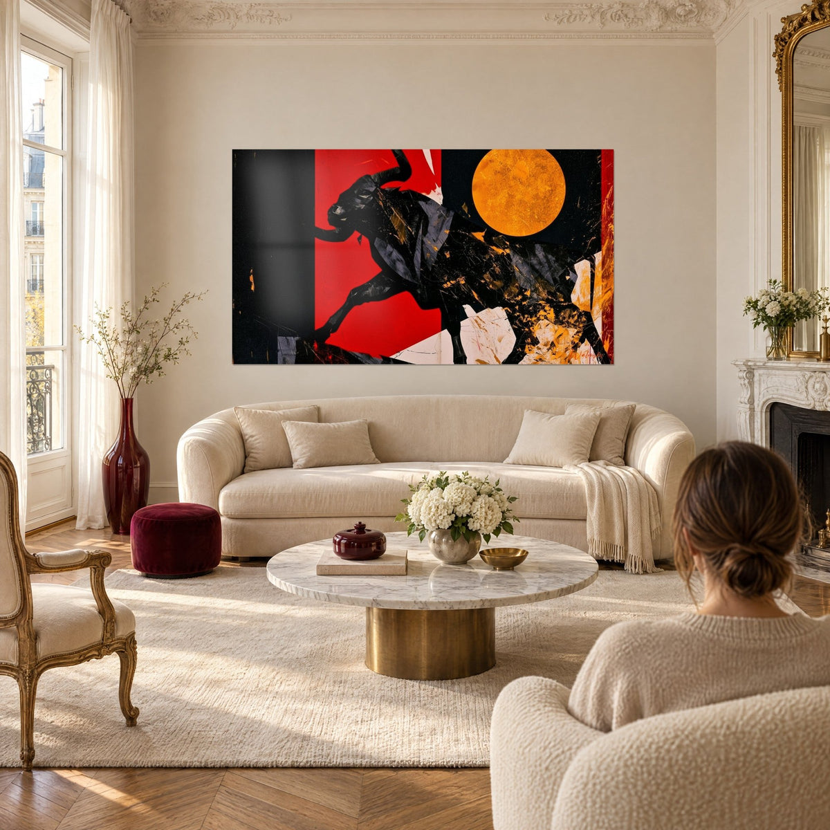 Wall art of a black bull leaping in front of a golden disc, vivid red background, woman seen from behind, above a sofa in a bright living room