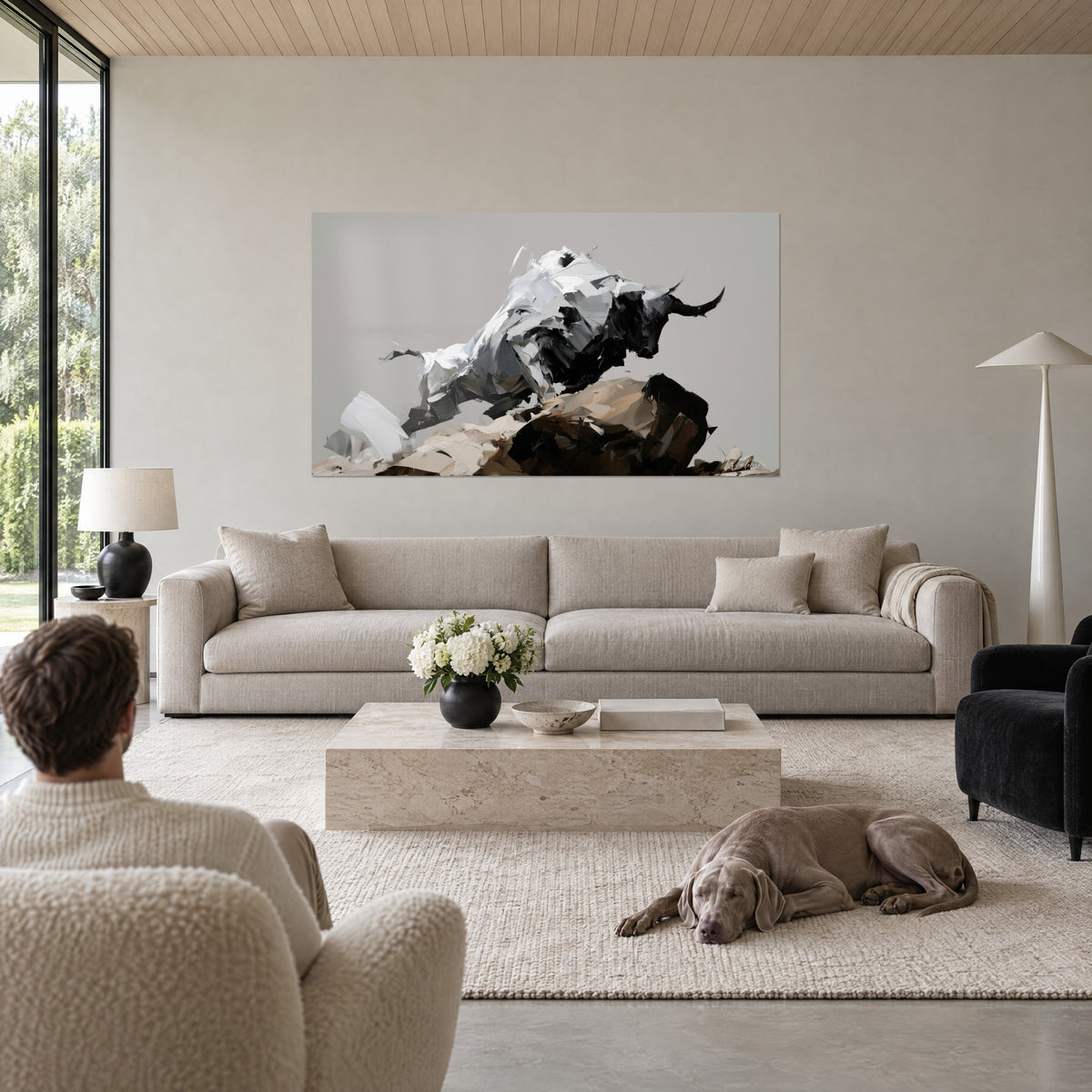 Wall art of a rearing bull with black horns, white and grey coat, palette-knife strokes on a brown mound, above a sofa in a bright living room