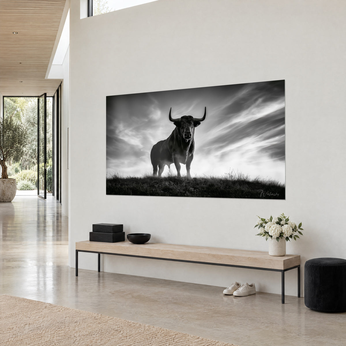 Cuadro de un imponente bovino erguido sobre su cresta, silueta de carbón y cielo gris perla surcado de velos, en la pared de una casa de arquitecto