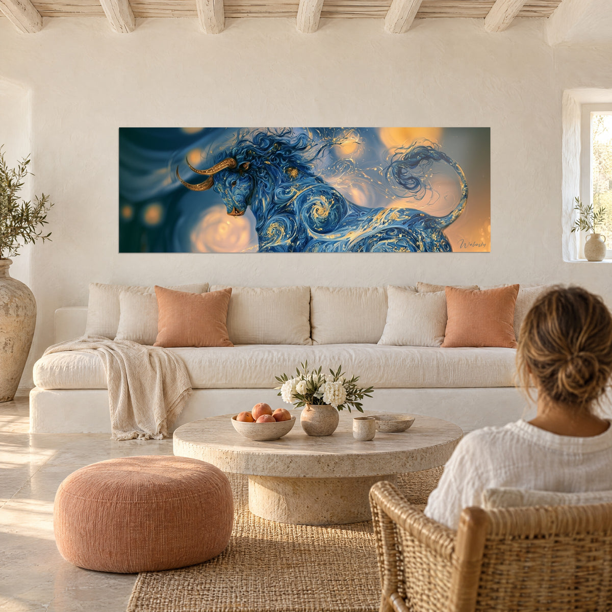 Wall art midnight blue longhorn with golden horns and swirling scrolls, a woman seen from behind, above a sofa in a bright living room