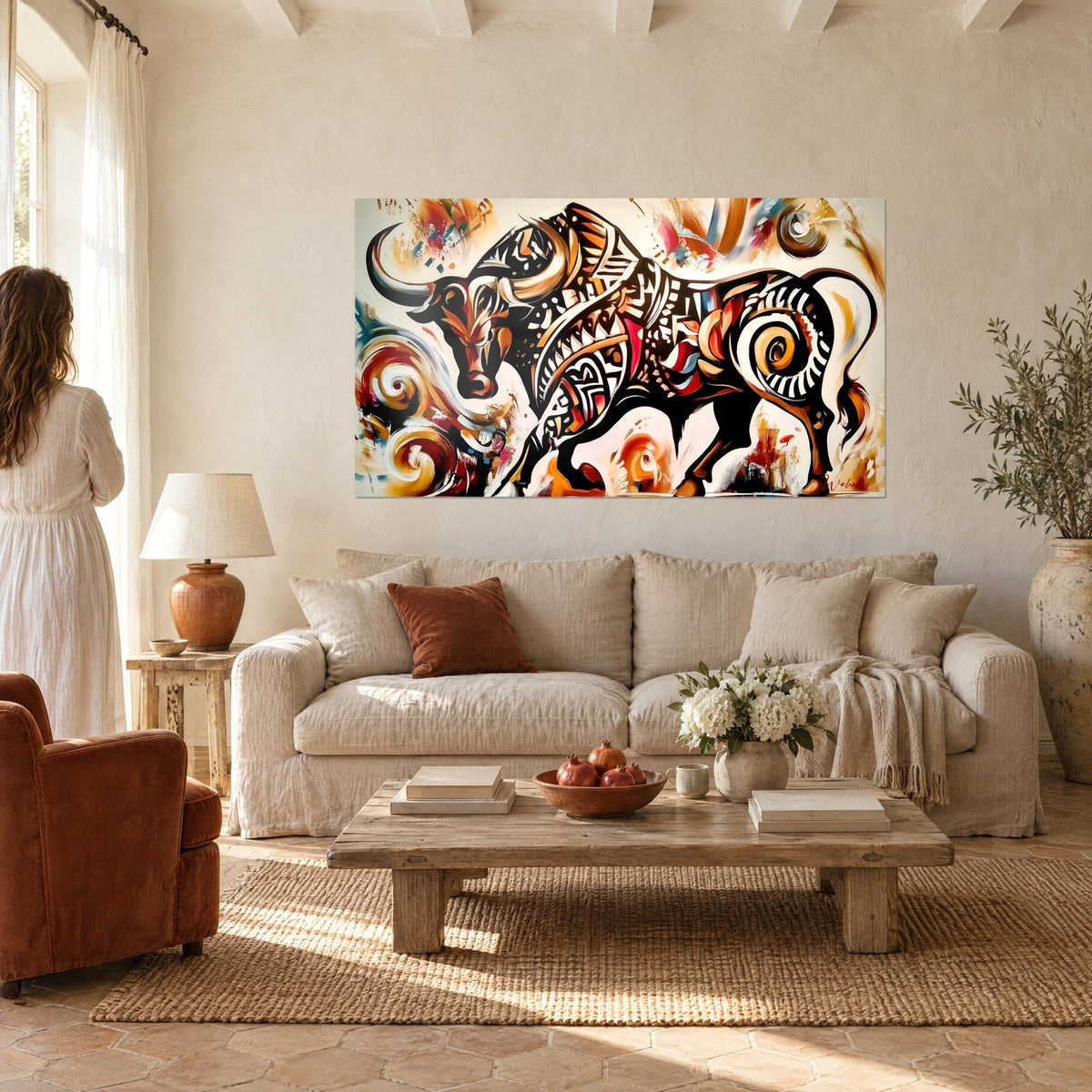 Quadro di un toro nero ricoperto di motivi tribali ocra e rossi, corna color crema, appeso sopra un divano in un soggiorno luminoso