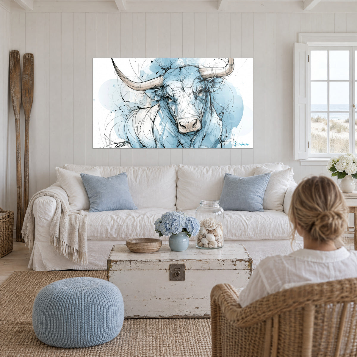 Tableau Longhorn aux cornes beige, encre bleu pâle et blanc, femme de dos, au-dessus d'un canapé dans un salon lumineux