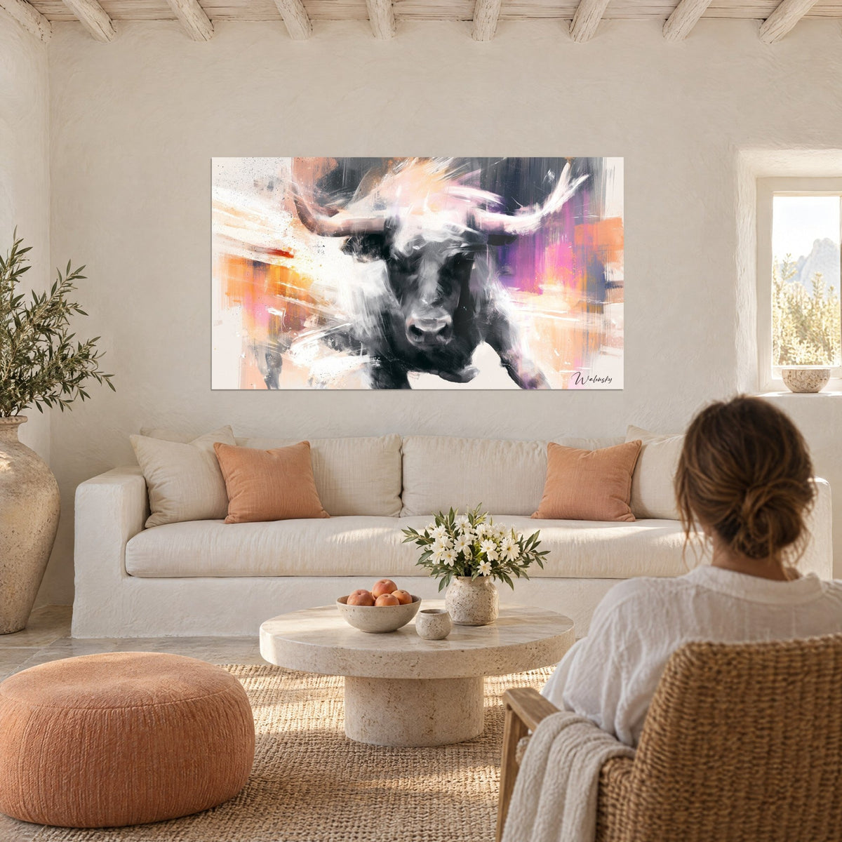 Wall art black Longhorn bull with ivory horns, purple and orange background, woman seen from behind above a sofa in a bright living room