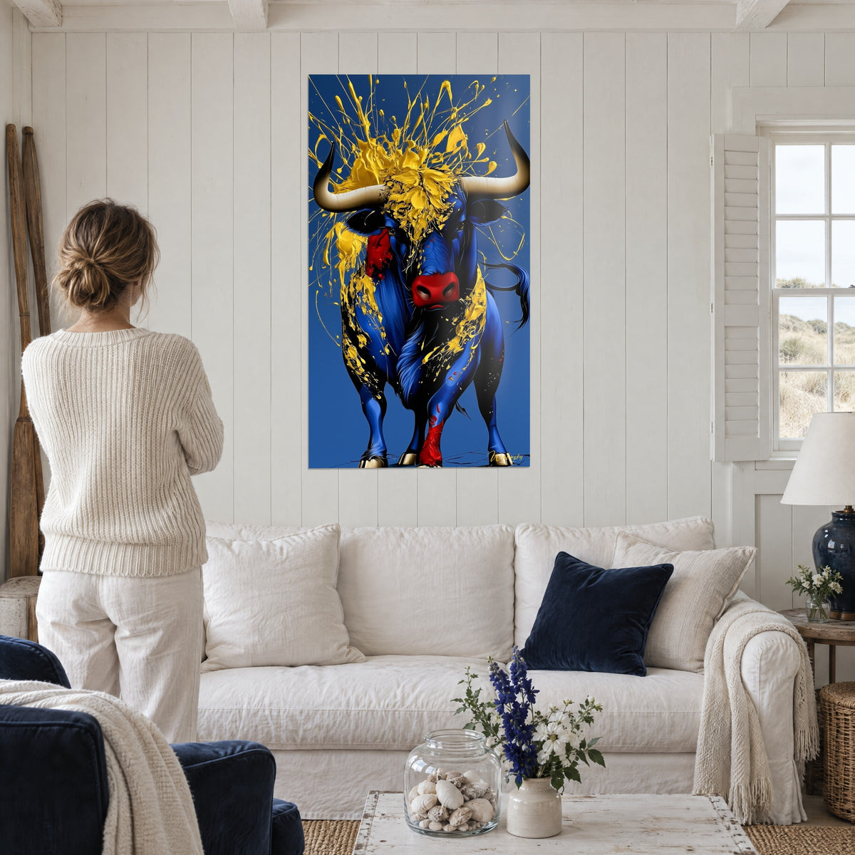 Schilderij van een kobaltblauwe stier met felgele spatten en rode snuit, boven een bank in een lichte woonkamer