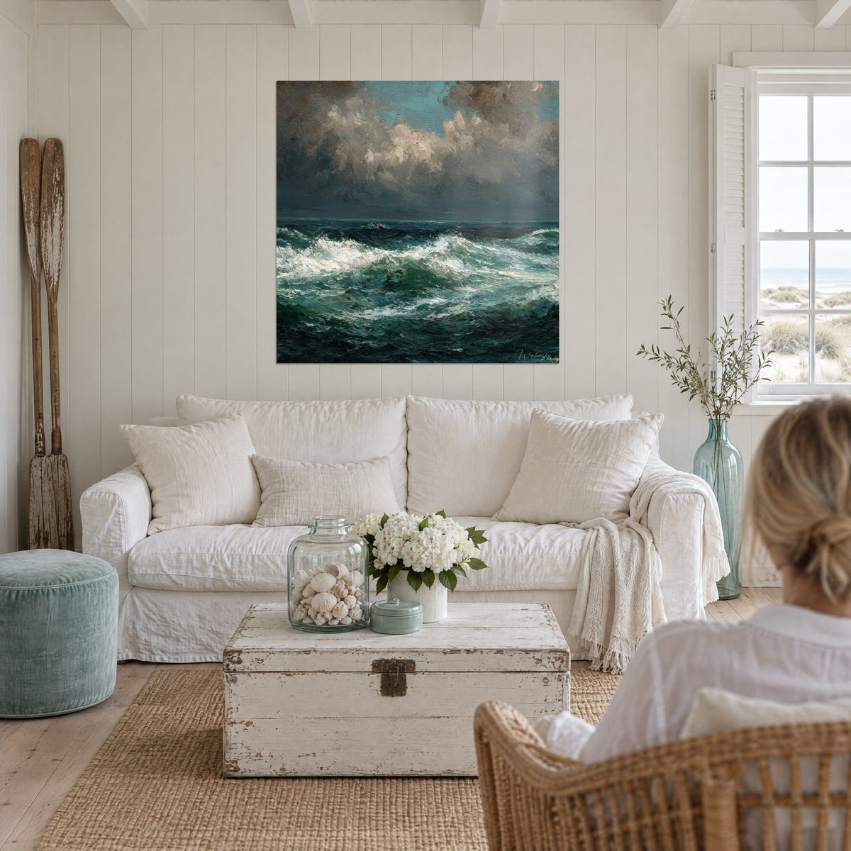 Wall art stormy sea with white foam crests under grey and brown clouds, two women seen from behind above a sofa in a bright living room