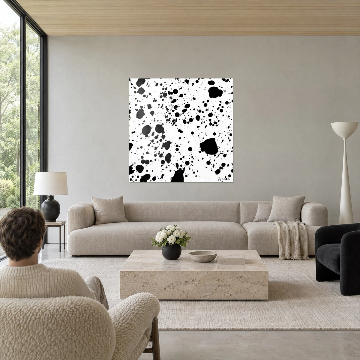 Gemälde mit schwarzen Tintenspritzern auf weißem Grund, große runde Flecken und feine Tropfen, über einem Sofa in einem hellen Wohnzimmer