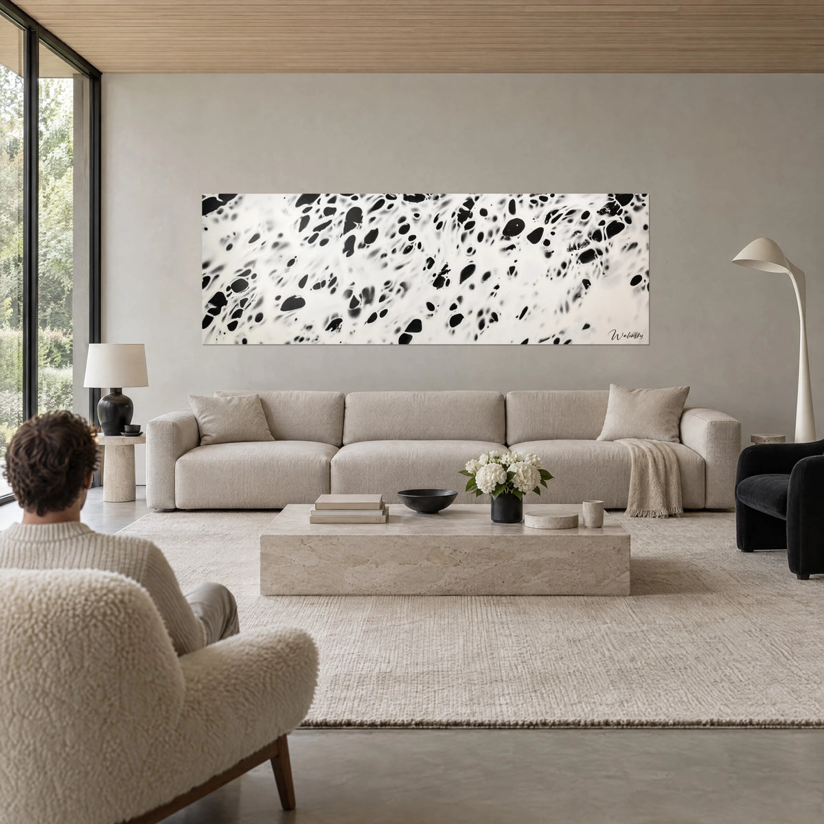 Tableau taches d'encre noires sur fond crème, silhouette de dos dans un fauteuil, au-dessus d'un canapé dans un salon lumineux
