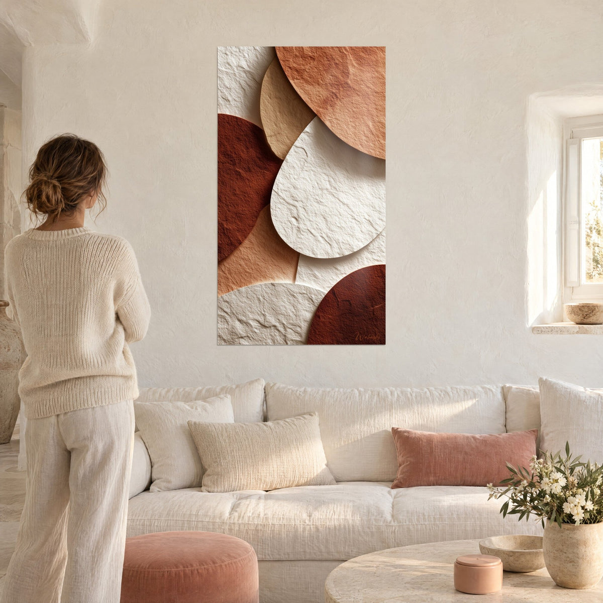 Gemälde mit zerknitterten Papierkieseln, weißen Ovalen und Ziegeltönen, eine Frau von hinten über einem Sofa in einem hellen Wohnzimmer