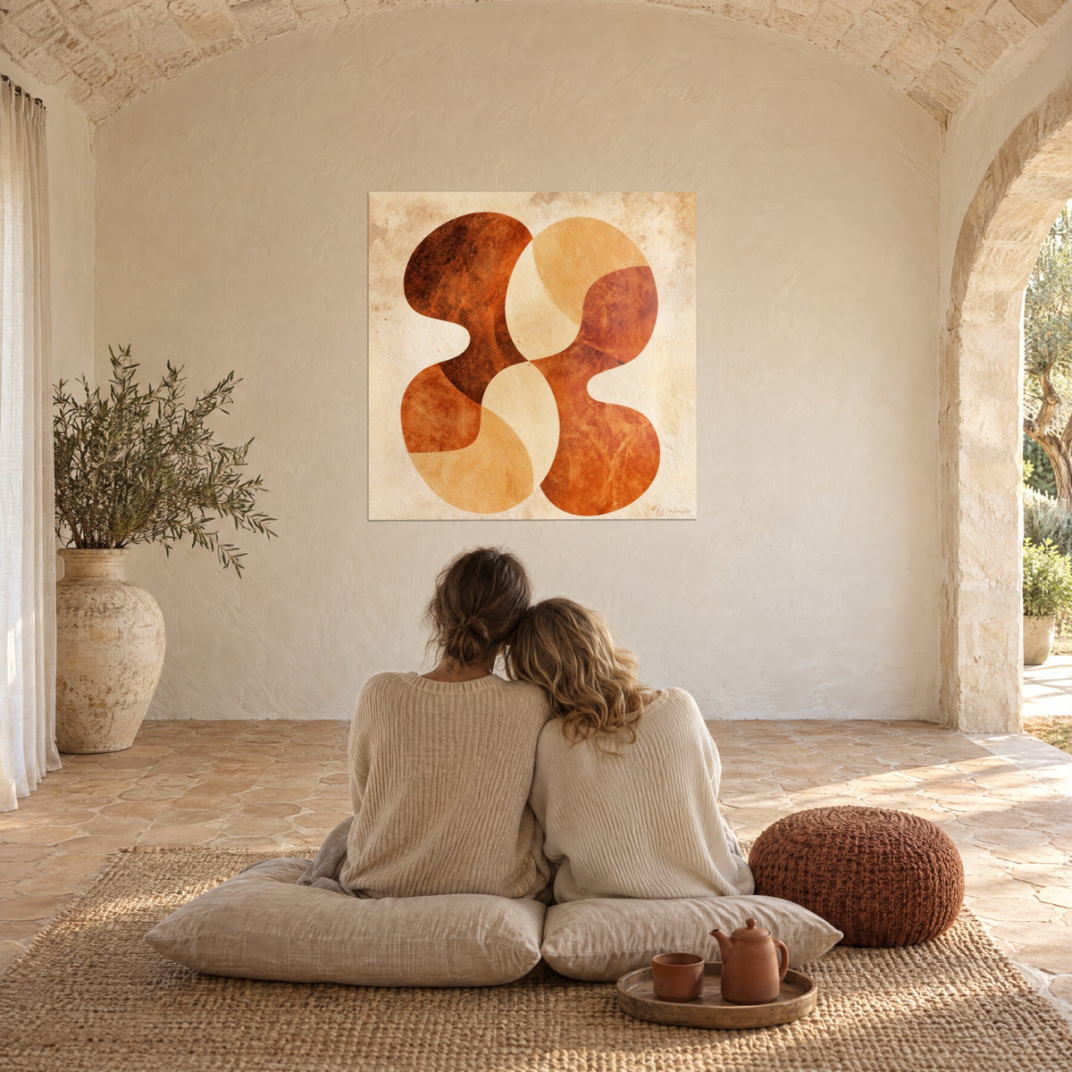 Quadro con fiore stilizzato dai petali caramello e cannella, coppia abbracciata di spalle su cuscini beige, pavimento in cotto in una sala a volta