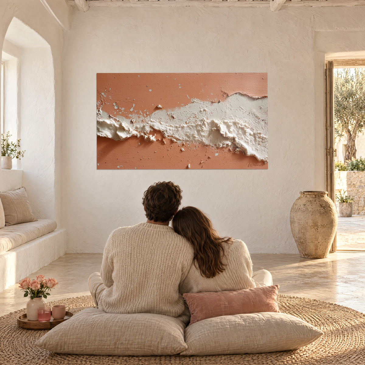 Tableau rivière de plâtre crème et corail rosé, texture épaisse, face à un couple sur des coussins en lin beige