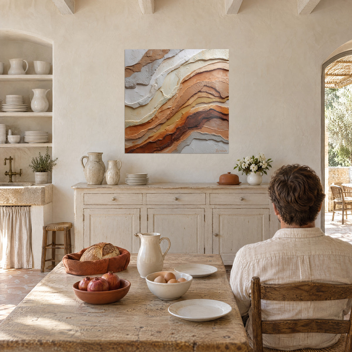 Quadro di paesaggio astratto di scogliere, strati grigi e terra di Siena, uomo di spalle seduto a un tavolo in una cucina provenzale soleggiata