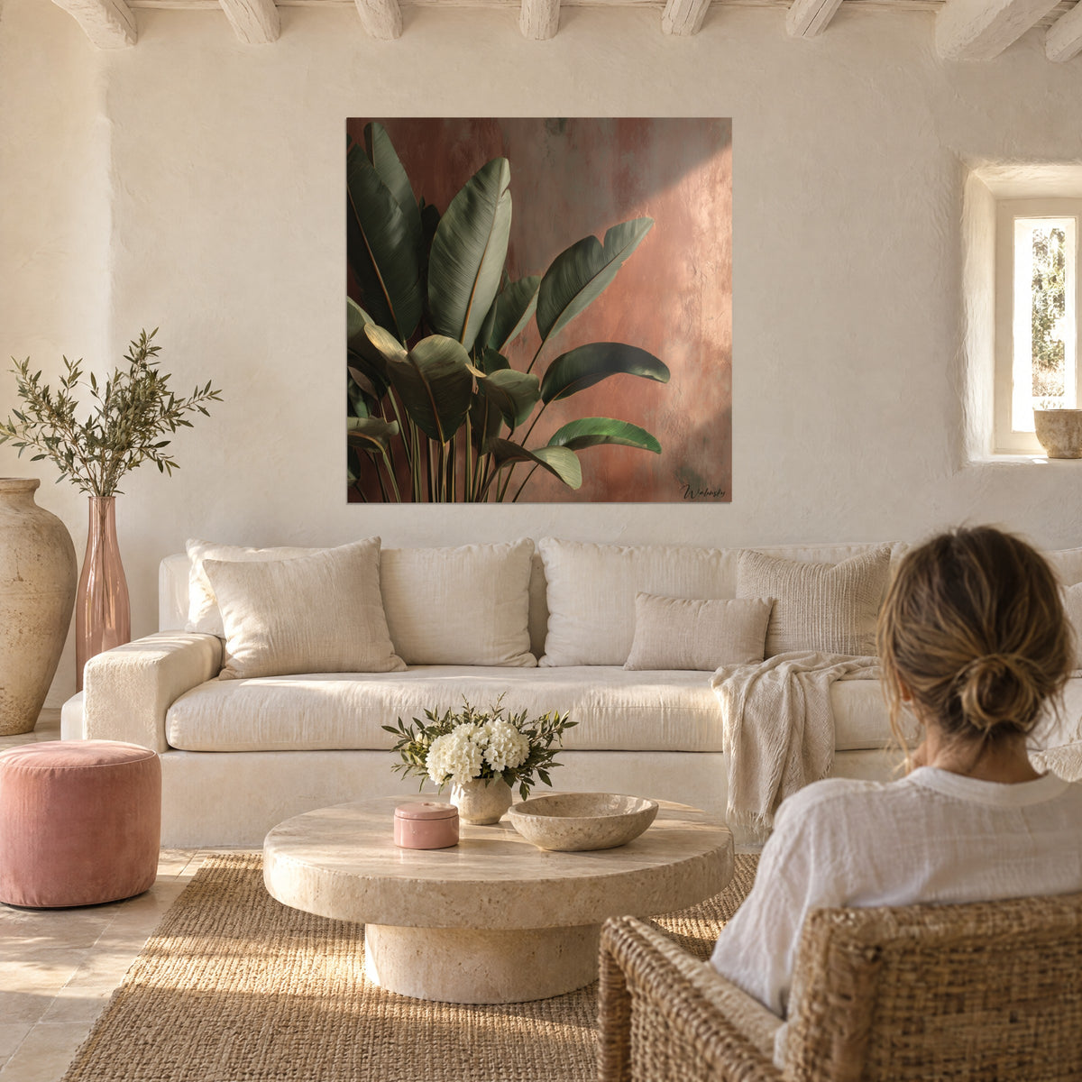 Tableau bananier aux larges feuilles vert olive devant un mur ocre rosé, couple de dos au-dessus d'un canapé dans un salon lumineux