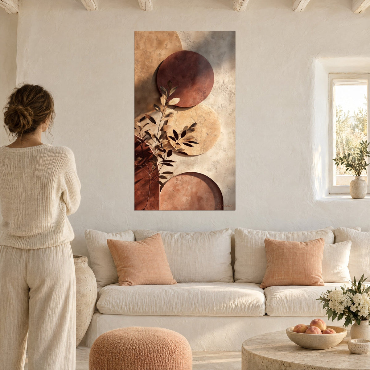 Tableau cercles terracotta et branche feuillue ocre, ombres portées sur crépi, femme de dos au-dessus d'un canapé dans un salon lumineux
