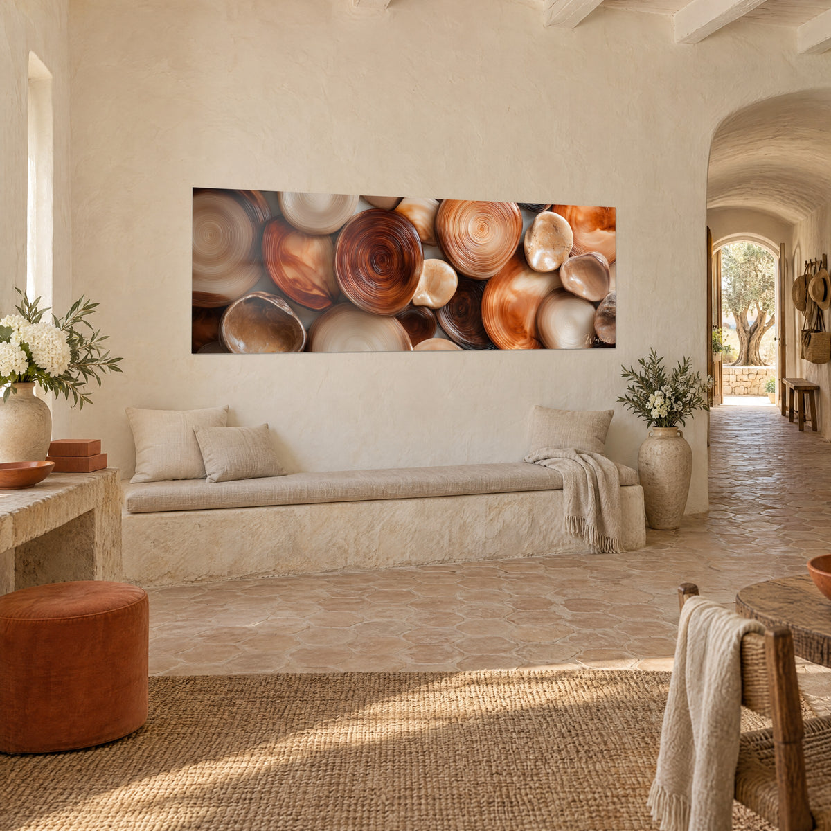 Quadro di pietre lisce in cerchi concentrici, arancio ramato e beige, su una parete di pietra chiara in un casale provenzale