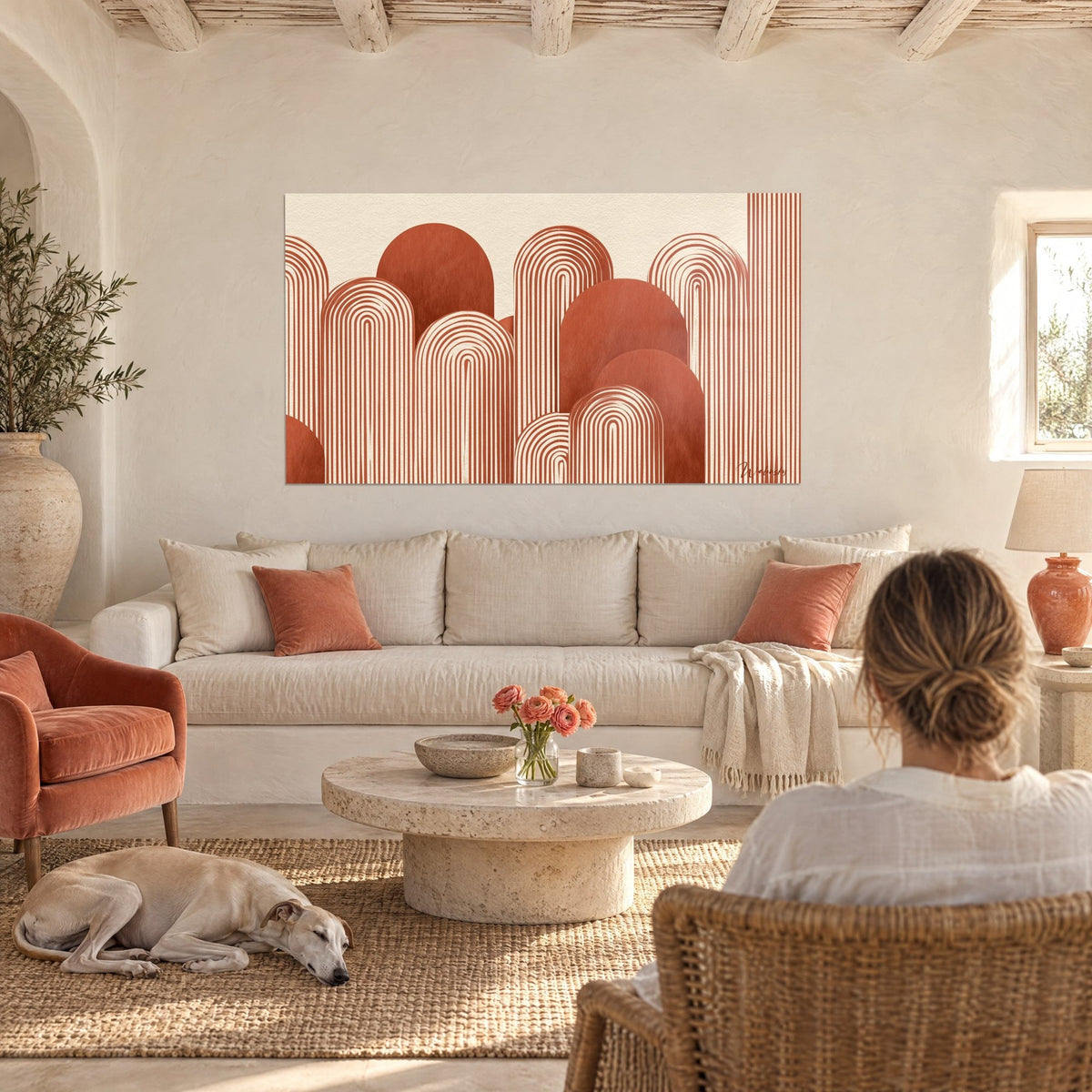Wall art with brick-red striped arches on a cream background, two people seen from behind and a greyhound, hung above a sofa in a bright living room