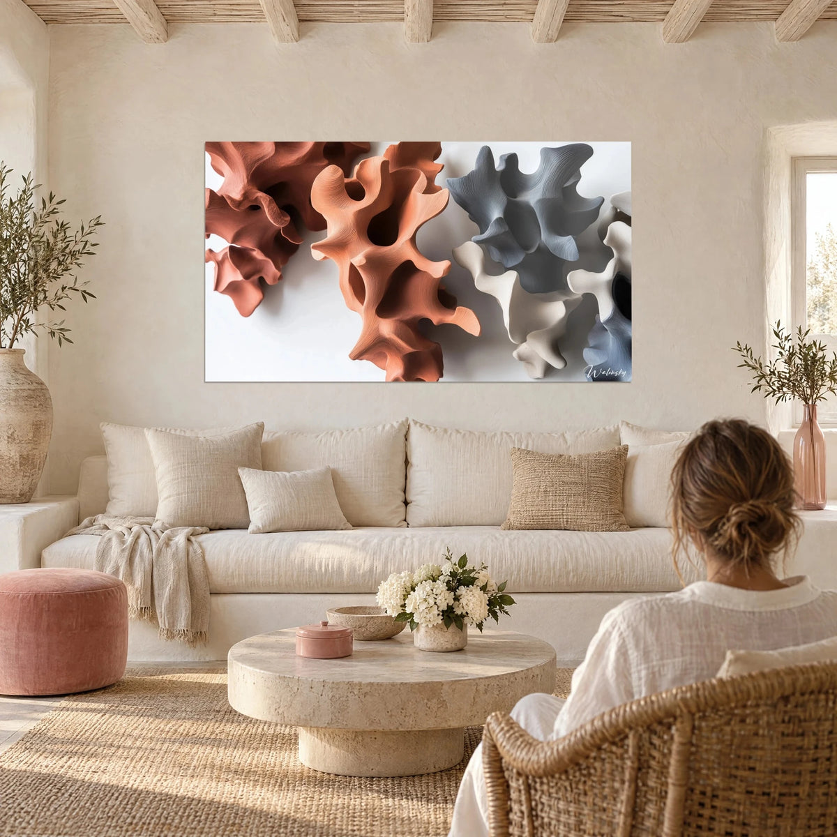 Wall art with coral-like sculptures in terracotta clay and slate grey, woman seen from behind, above a sofa in a bright living room
