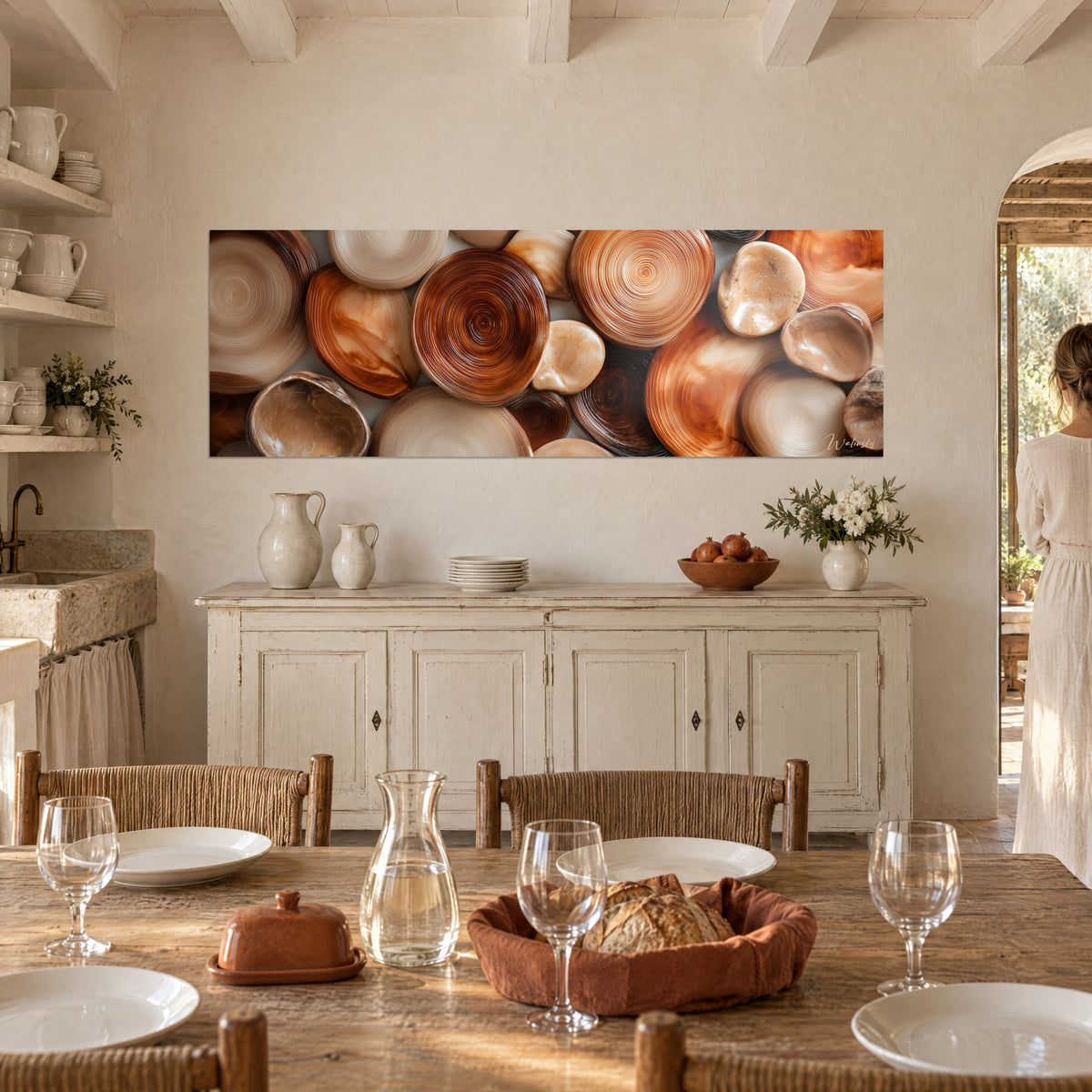 Quadro di pietre arrotondate con striature circolari, ambra e avorio, donna di spalle vicino a una credenza bianca e a un tavolo in legno