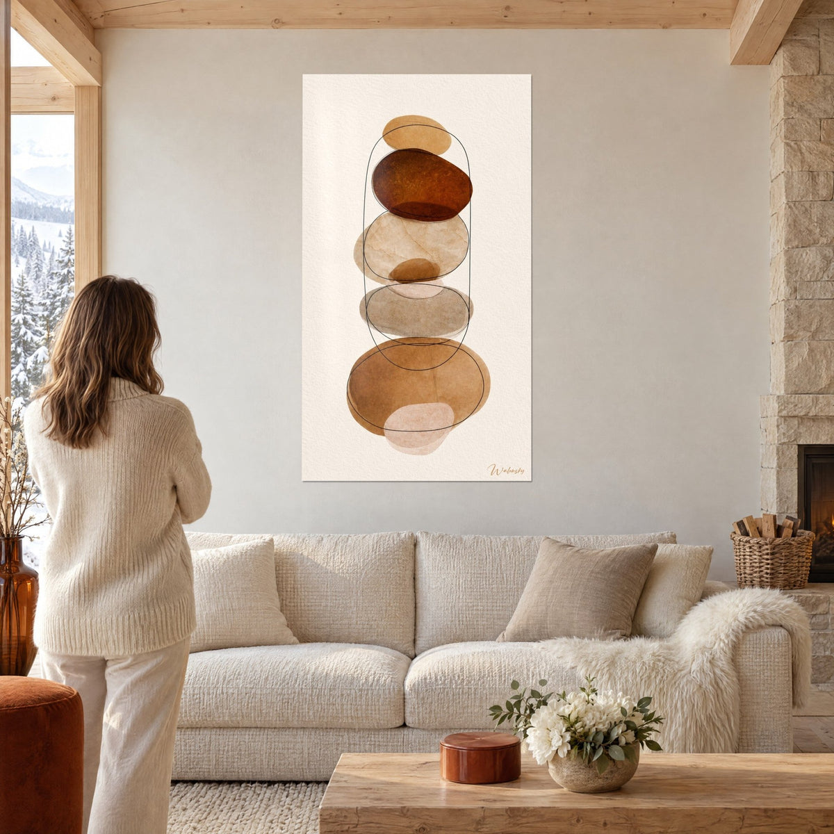 Quadro ciottoli impilati in bruno ramato e beige sabbia, contornati da un tratto nero ovale, coppia di spalle sopra un divano in un soggiorno luminoso