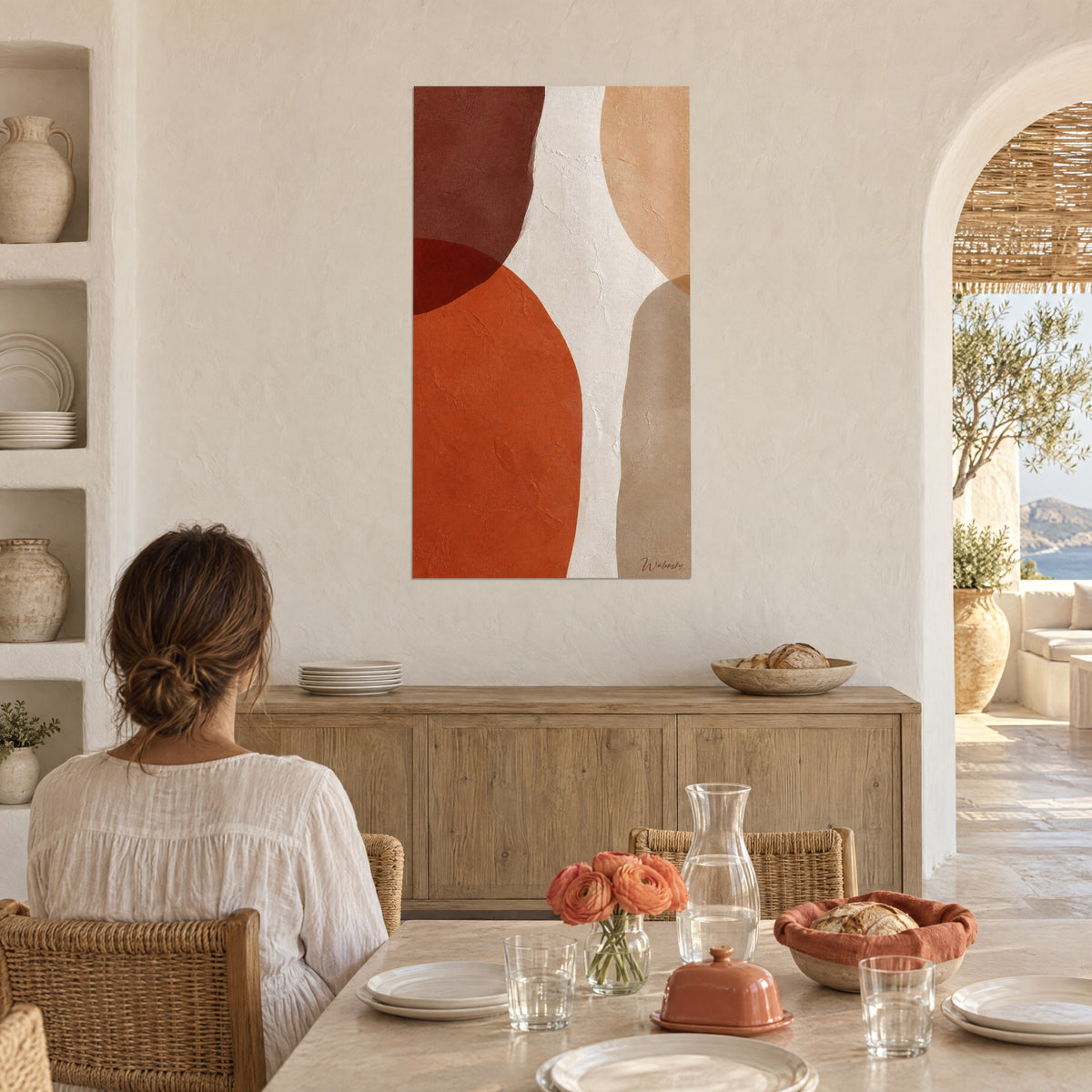 Πίνακας με αφηρημένα οβάλ σε ώχρα, κόκκινο καφέ και κρεμ με υφή, γυναίκα από την πλάτη σε τραπέζι, σε μεσογειακό σπίτι κοντά σε αψίδα