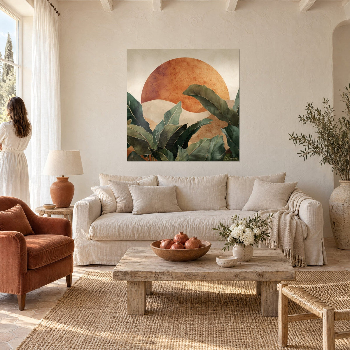 Wall art of sage green banana leaves in front of a large terracotta sun, woman seen from behind, above a sofa in a bright living room