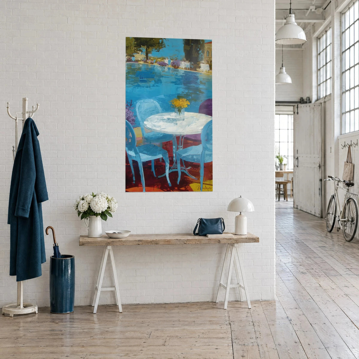 Tableau chaises bleu ciel autour d'une table blanche, fleurs jaunes et dalles rouges, vue de trois-quarts sur une console de loft