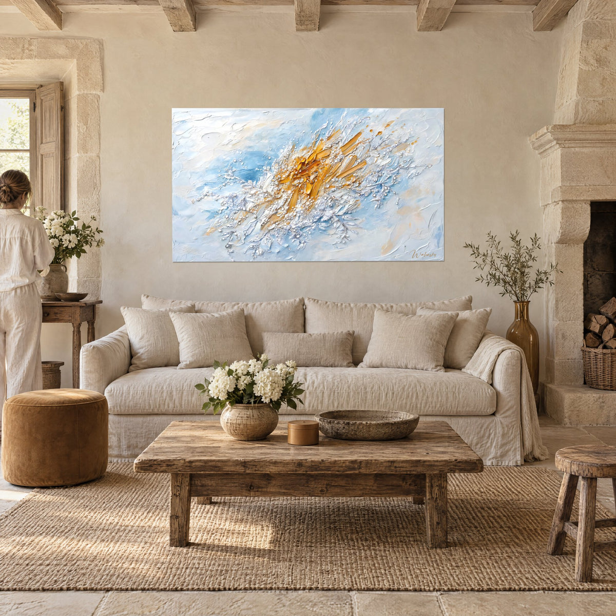 Tableau gerbe d'or éclatante sur fond bleu pastel, empâtements blancs, une femme de dos, au-dessus d'un canapé dans un salon lumineux
