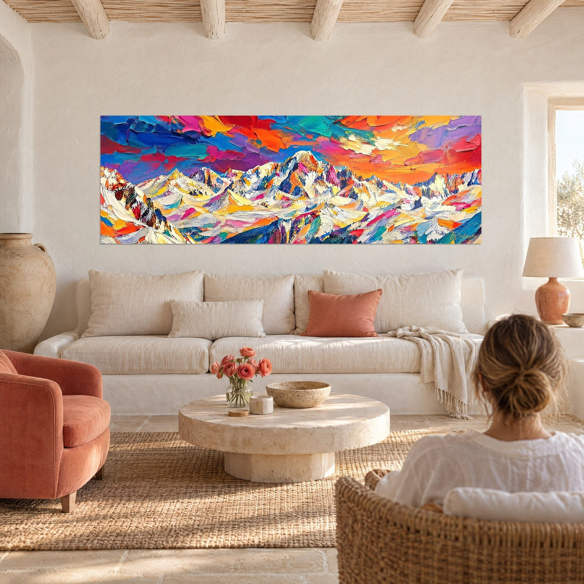 Tableau massif enneigé sous ciel orange et violet, empâtements turquoise et rose, femme de dos, au-dessus d'un canapé dans un salon lumineux