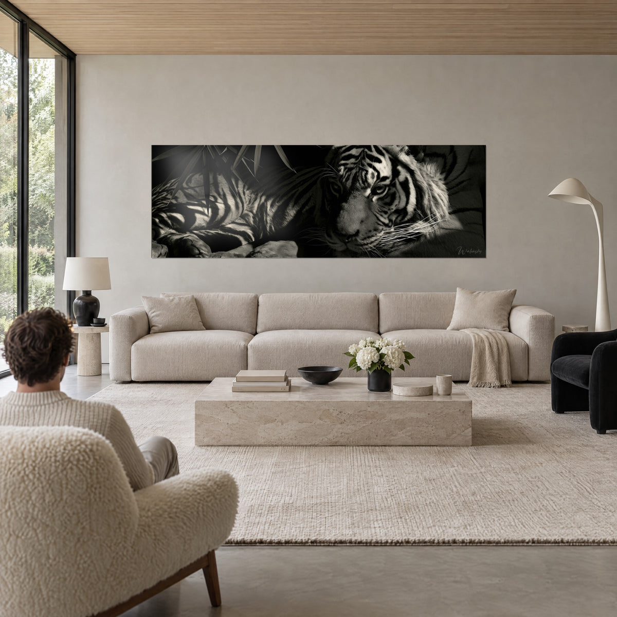 Tableau tigre allongé en noir et blanc, regard ambre, feuilles de bambou sombres, personne de dos au-dessus d'un canapé dans un salon lumineux