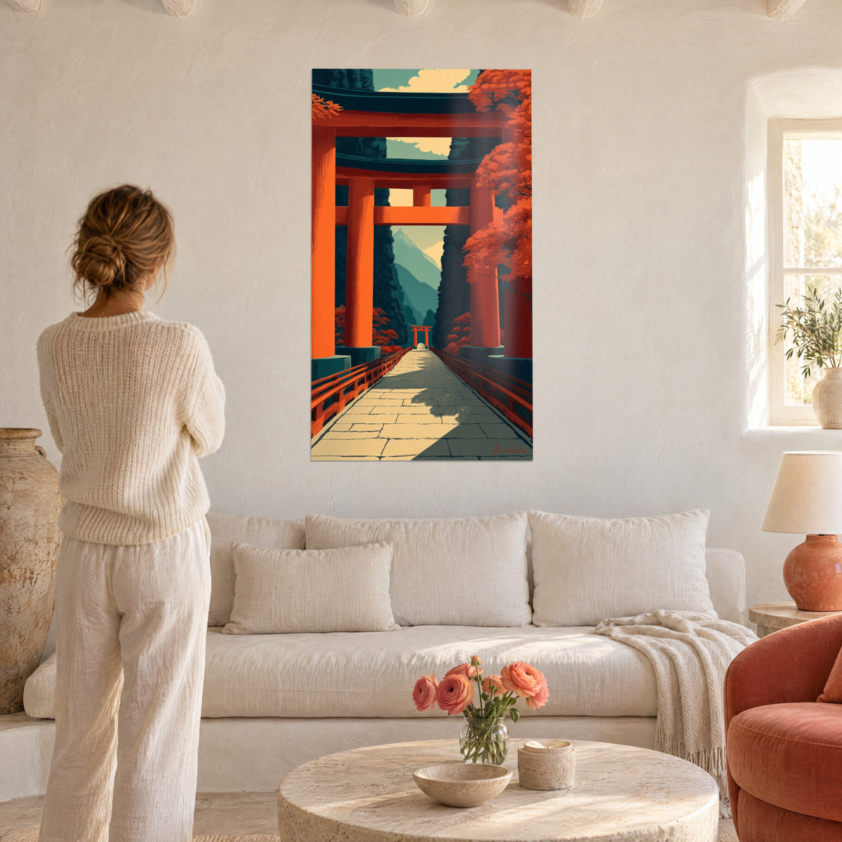 Wall art vermilion torii gate over a paved path, red maple trees and bluish mountain peak, woman seen from behind, above a sofa in a bright living room